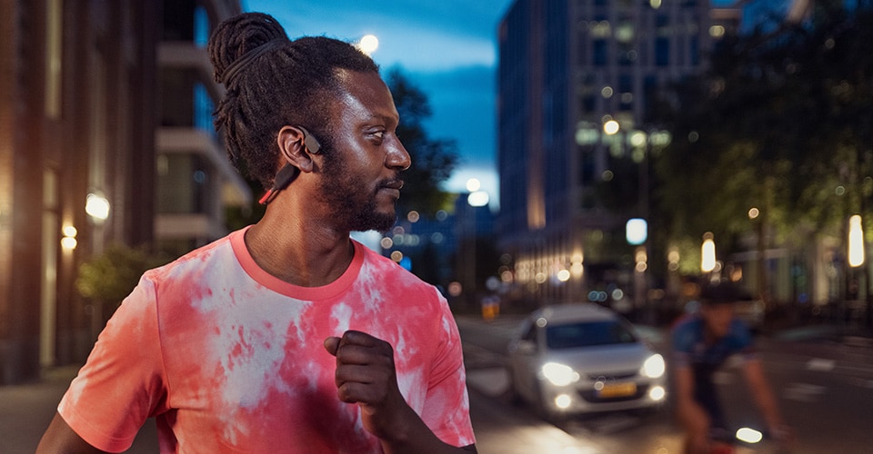 Atleta usando auriculares de conducción ósea en una calle muy transitada